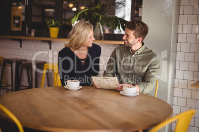 Smiling young man and woman sitting with coffee cups at cafe