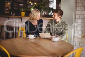 Smiling young man and woman sitting with coffee cups at cafe