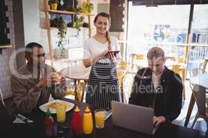 Portrait of smiling waitress holding tablet while standing by young customers