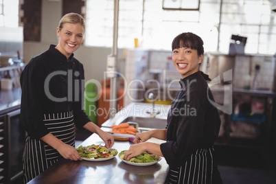 Smiling female chefs with fresh food in plates on kitchen counter