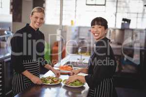 Smiling female chefs with fresh food in plates on kitchen counter