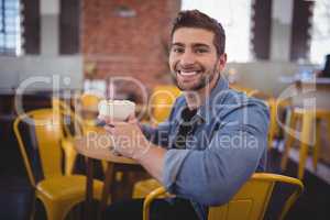 Portrait of smiling handsome man holding fresh coffee cup at cafe