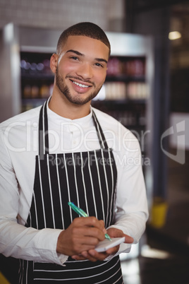 Portrait of smiling young waiter standing with notepad and pen