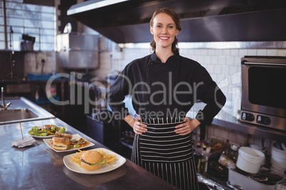 Portrait of smiling young waiter standing with hands on hip by food