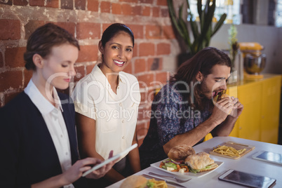 Portrait of smiling young woman sitting amidst friends at table with food