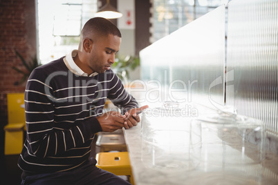 Young man text messaging through smartphone while sitting at counter