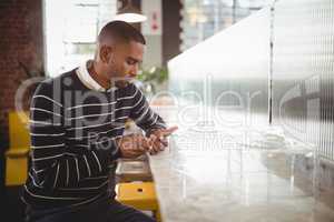 Young man text messaging through smartphone while sitting at counter