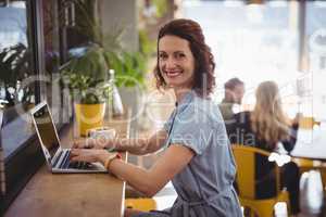 Smiling young woman using laptop while sitting at counter