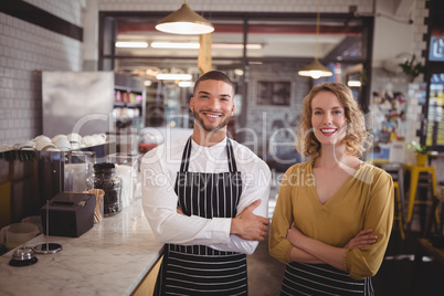 Portrait of smiling young wait staff standing with arms crossed by counter