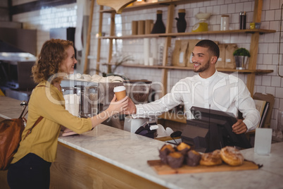 Smiling waiter giving disposable coffee cup to young female customer at counter