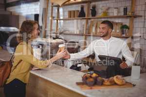 Smiling waiter giving disposable coffee cup to young female customer at counter