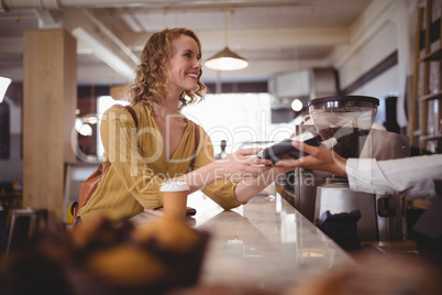 Smiling beautiful female customer paying through card at counter