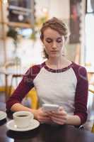 Beautiful woman using mobile phone while sitting at table with coffee cup