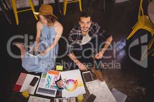 High angle portrait of smiling young male designer sitting by female colleague with sheets