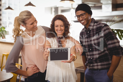 Smiling woman taking selfie with friends from digital tablet at coffee shop