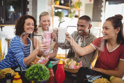 Happy young friends raising drinks while sitting at coffee shop