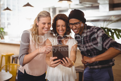 Cheerful multi ethnic friends taking selfie from digital tablet at coffee shop