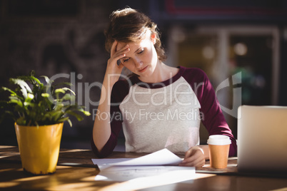 Troubled young female designer reading paper at coffee shop