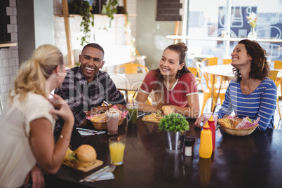 Young friends talking while sitting at table with food and drink