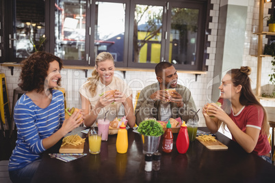 Smiling young friends eating food while sitting at coffee shop