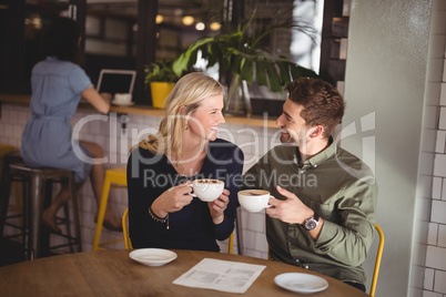 Smiling couple holding fresh coffee cups while sitting at cafeteria