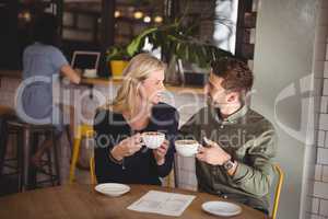 Smiling couple holding fresh coffee cups while sitting at cafeteria