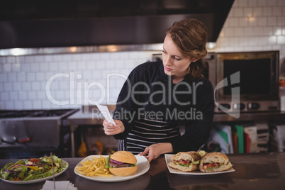 Confident young waiter holding paper while standing with fresh meal at counter