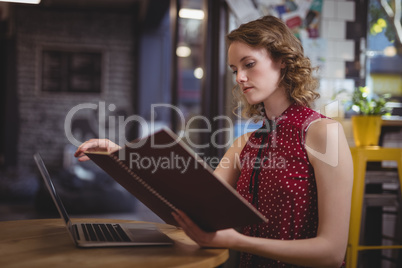 Beautiful young woman reading document while sitting at coffee shop