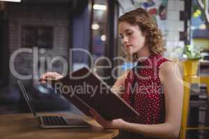 Beautiful young woman reading document while sitting at coffee shop