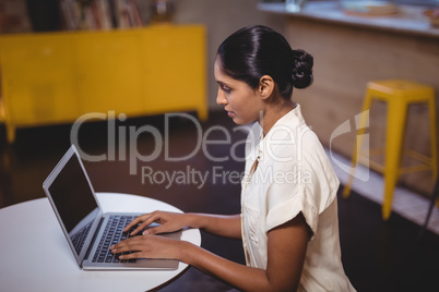 Side view of young woman typing on laptop while sitting at coffee shop
