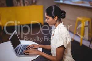Side view of young woman typing on laptop while sitting at coffee shop