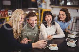 Cheerful friends using digital tablet while sitting at coffee shop