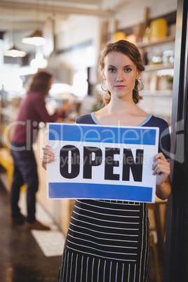 Portrait of confident young waitress holding open sign placard
