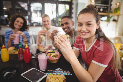 Portrait of smiling young friends sitting with food and drink