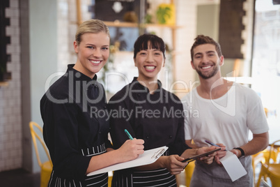 Portrait of cheerful young wait staff holding digital tablet with notepad and clipboard