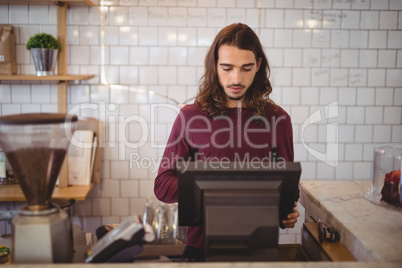 Young waiter with long hair using cash register at coffee shop