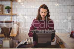Young waiter with long hair using cash register at coffee shop