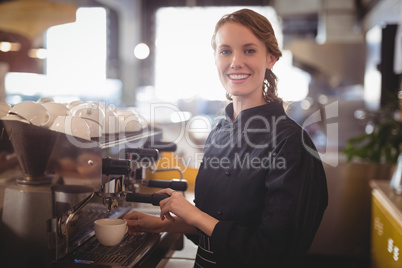 Portrait of smiling young waitress using espresso maker
