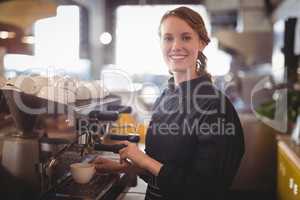 Portrait of smiling young waitress using espresso maker