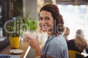 Portrait of smiling woman holding fresh coffee at cafe
