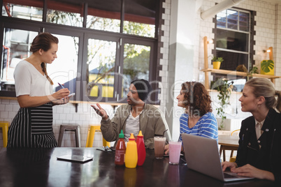 Young man sitting with friends ordering food to waitress