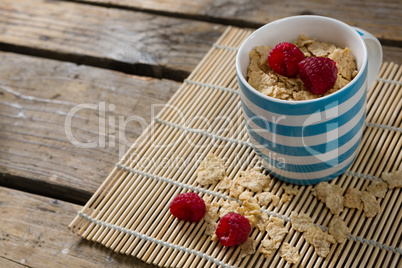 Flakes with raspberries in mug on place mat