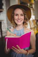 Portrait of smiling young woman holding pink dairy with pen