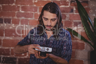 Confident young male photographer using camera against brick wall