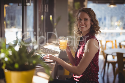 Side view portrait of smiling young woman holding fresh juice glass at coffee shop