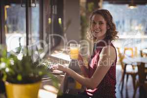 Side view portrait of smiling young woman holding fresh juice glass at coffee shop