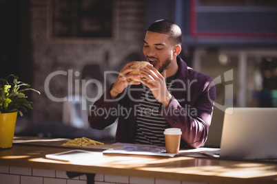 Young male professional eating burger at coffee shop