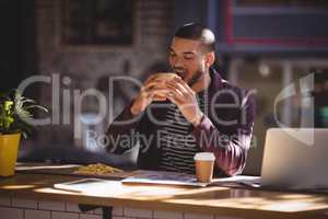 Young male professional eating burger at coffee shop