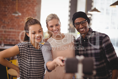 Young woman taking selfie with friends from mobile phone at coffee shop