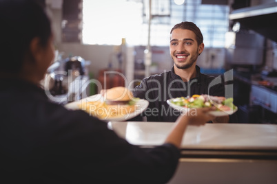 Smiling young waiter giving food to waitress at counter